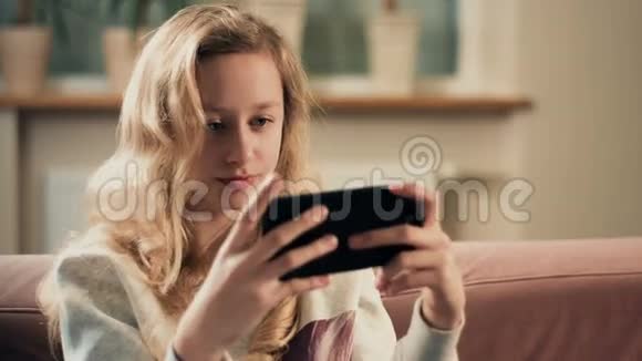 女孩在智能手机上玩游戏放学后在家休闲活动视频的预览图