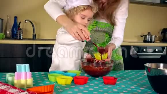 妈妈和可爱的小女儿一边微笑一边装满五颜六色的松饼盒视频的预览图