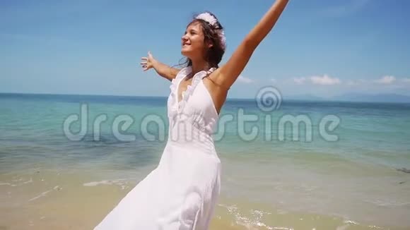 穿着白色连衣裙和花圈的布鲁内特年轻女子光着脚在海岸边奔跑享受着旋转的乐趣视频的预览图