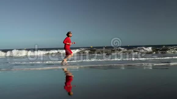 日落时分穿着红色裙子的快乐年轻女子沿着海边奔跑无忧无虑的现代生活理念视频的预览图