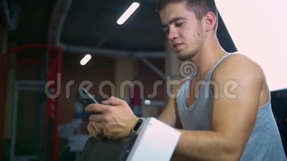 运动员锻炼后坐在健身中心在网上聊天智能手机视频的预览图