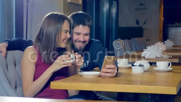 漂亮的年轻夫妇带着智能手机使用新的应用程序一起笑视频的预览图