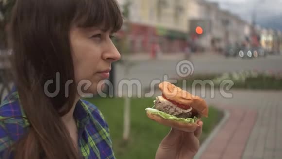 一个女人在一条繁忙的马路旁边的街道上咬一个汉堡的画像视频的预览图