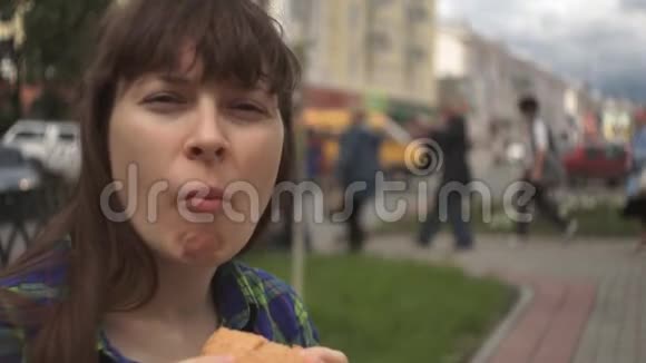 一个女人在一条繁忙的马路旁边的街道上咬一个汉堡的画像视频的预览图
