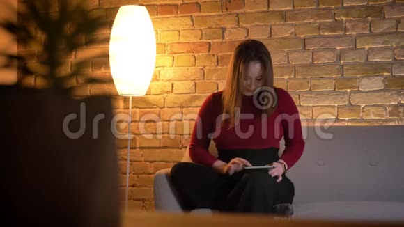年轻漂亮的白种人女性在平板电脑上打字的特写镜头坐在室内的沙发上视频的预览图