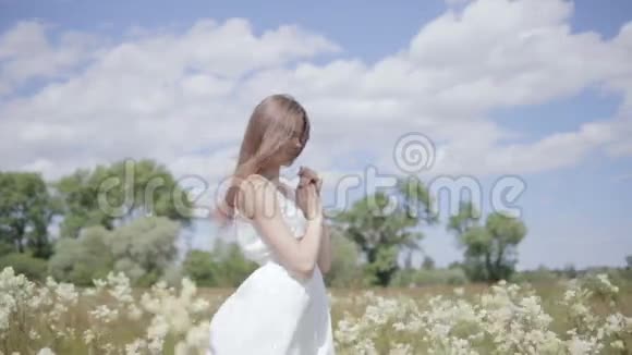 花丛中的年轻漂亮的女人低头看着头发上的风视频的预览图