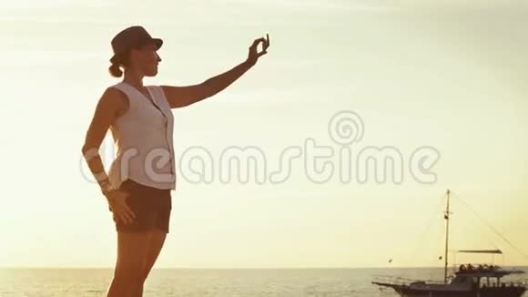 可爱的女孩用日落的海洋背景给自己拍照视频的预览图