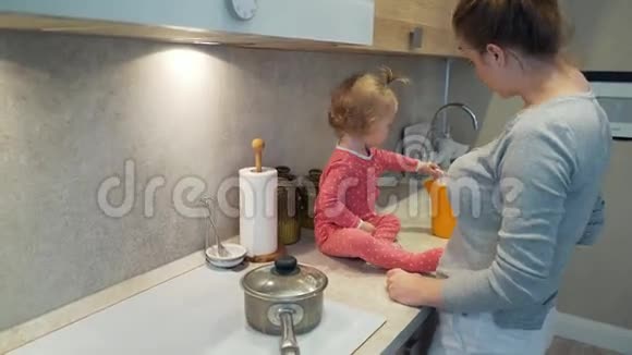快乐的年轻妈妈和一个坐在厨房桌子上的孩子一起做饭视频的预览图