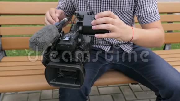 坐在长凳上的摄影师浏览了电视摄像机的镜头视频的预览图