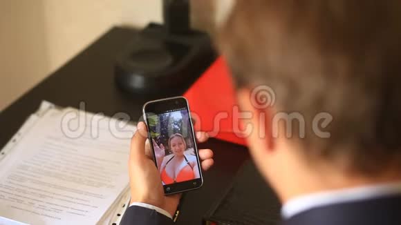 一个穿西装的商人坐在办公桌前的办公室里和海滩上的一个女孩举行视频聊天她穿着视频的预览图