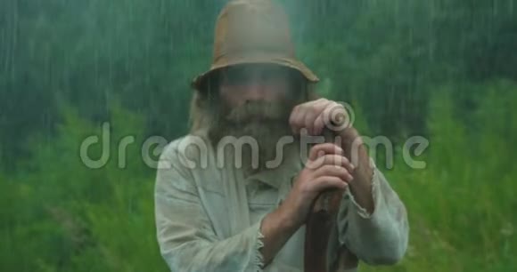 特写肖像的老人留着长长的胡须穿着旧衣服在雨中一边嚼着拐杖视频的预览图