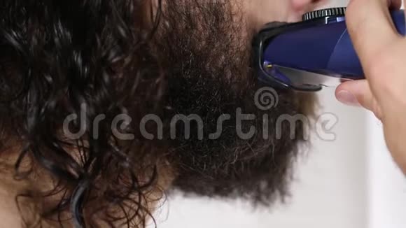 英俊的年轻人留着长发在浴室里用修剪器刮胡子特写镜头视频的预览图