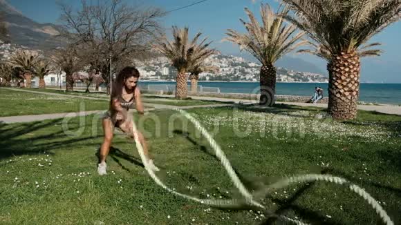 女人用两根绳子抱在怀里做运动快速地站在户外的草地上视频的预览图
