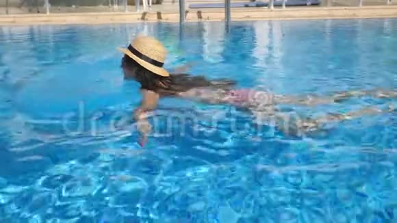 年轻漂亮的女孩戴着太阳镜和帽子在游泳池游泳在阳光明媚的日子里女人在清澈的温水中放松夏季视频的预览图