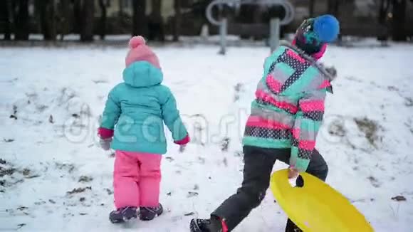 两个穿着五颜六色衣服的小妹妹喜欢下雪的天气和雪橇正试图爬上山有趣的女孩视频的预览图