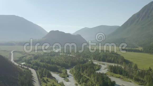 空中无人机景在日落柔和的光线下飞越松树林山河和乡村道路山区视频的预览图