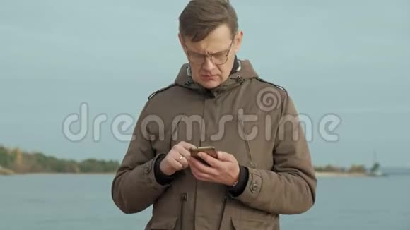 成熟的商人坐在河边放松穿暖和夹克用智能手机的人视频的预览图