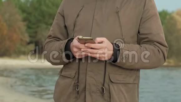 成熟的商人坐在河边放松穿暖和夹克用智能手机的人视频的预览图