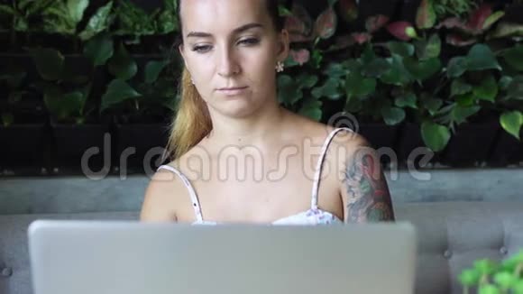 有纹身的女人在咖啡店用笔记本电脑纹身的女性在咖啡馆的电脑上在线工作视频的预览图