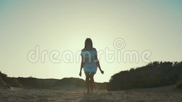 穿着白色连衣裙的女孩在日落背景下跳跃沙漠慢动作视频的预览图