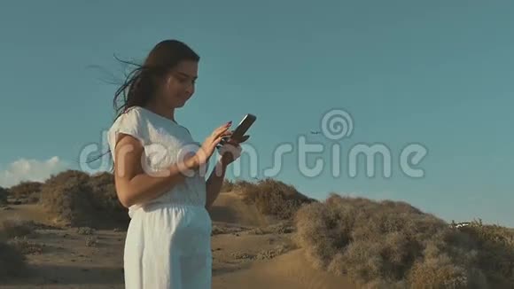 穿着白色衣服的女孩在打电话空中飞机日落在沙漠里温暖的夏日傍晚沙漠慢慢视频的预览图
