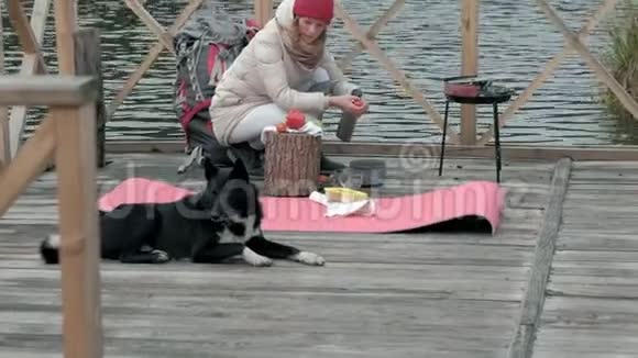 一位穿着温暖衣服的女游客在河岸附近的一座桥上背着一个背包一只狗在旁边玩耍做饭视频的预览图