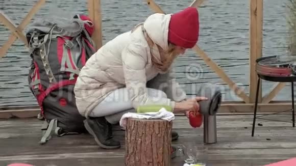 一位穿着温暖衣服的女游客在河岸附近的一座桥上背着一个背包一只狗在旁边玩耍做饭视频的预览图