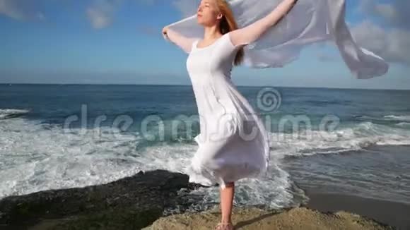 自由概念穿着白色连衣裙和围巾的女人站在岩石上跳舞在飞行移动做体操视频的预览图