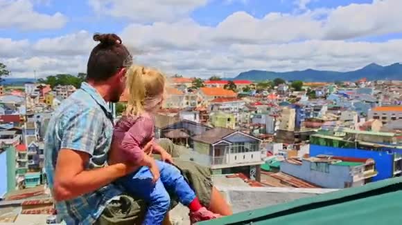 亲密父亲小女孩坐在屋顶挥手看城市视频的预览图