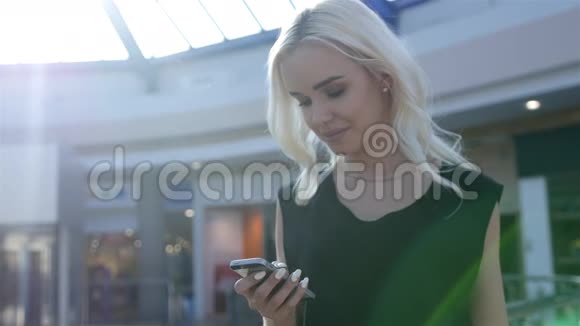 一个女孩站在购物中心的自动扶梯旁等待朋友并在电话中交谈学生妇女时尚模特视频的预览图