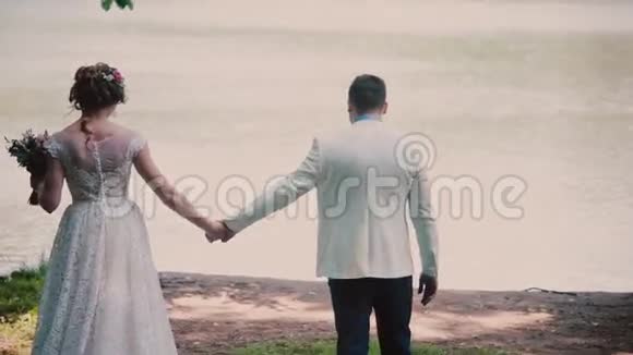 婚礼当天一对幸福的夫妇牵着手走在河岸上漂亮的白色衣服视频的预览图