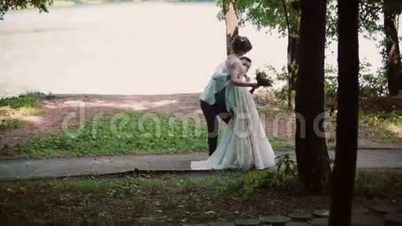 英俊的新郎把新娘抱在怀里旋转着夏天在河岸上举行美丽的婚礼视频的预览图
