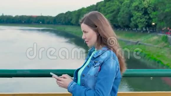 穿着棉袄穿过河上的桥用智能手机的漂亮女孩视频的预览图