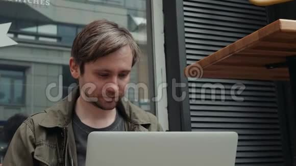 在面包店休息的时候用手提电脑在社交网络上与朋友重写白人男子的微笑视频的预览图