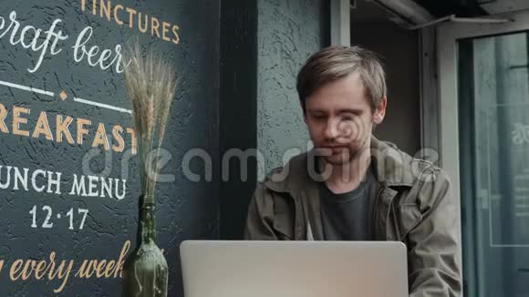 在面包店休息的时候用手提电脑在社交网络上与朋友重写白人男子的微笑视频的预览图