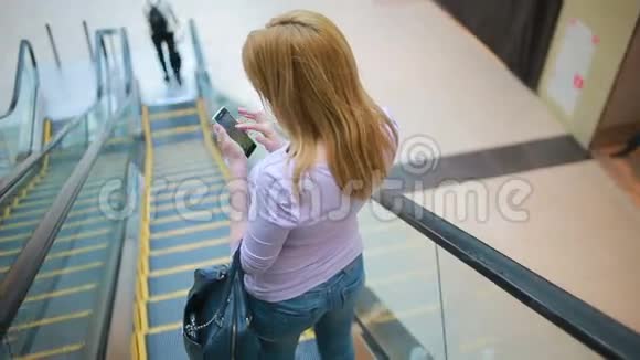 年轻的金发女人坐在地下自动扶梯上用智能手机视频的预览图