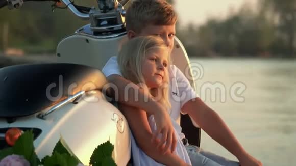 哥哥和姐姐坐在海边日落时的脚踏车上哥哥拥抱妹妹儿童席视频的预览图