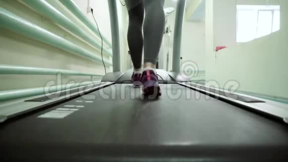 漂亮的白种人女孩在运动健身房的跑步机上跑步脚特写视频的预览图