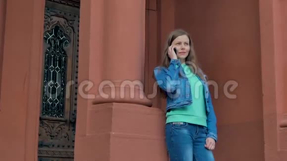 穿着棉袄在智能手机上说话的漂亮女孩背景中的老式建筑视频的预览图