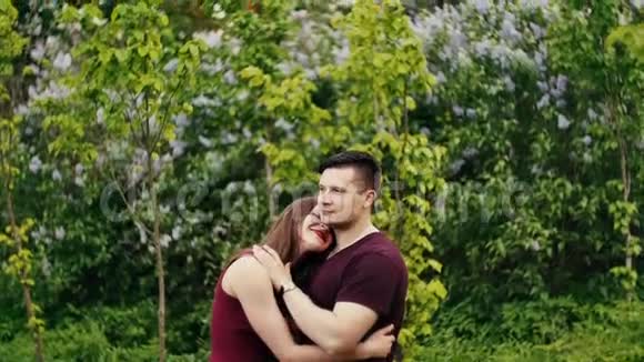 美丽的女人靠在她的男人的肩膀上因为他们站在丁香灌木丛附近相爱的幸福夫妻慢节奏视频的预览图