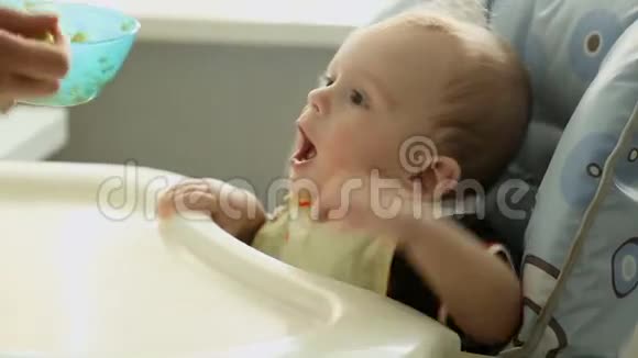饥饿的一岁男孩在厨房的高椅上吃粥视频的预览图