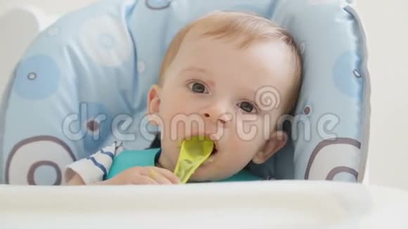 一岁的小男孩坐在高椅上用勺子吃粥视频的预览图