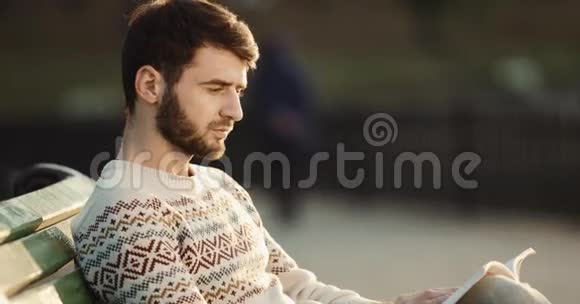 年轻人坐在公园里的长凳上看书高清高清视频的预览图