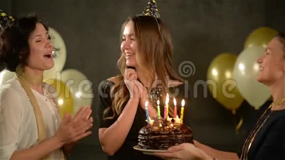 两个女人在帽子里唱生日快乐歌给他们的朋友和一个巧克力蛋糕令人惊奇的女士吹蜡烛视频的预览图