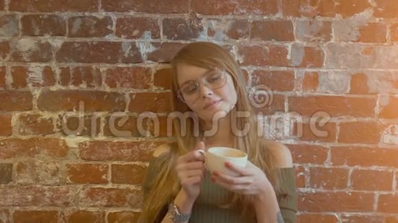 美丽的年轻微笑的女人端着一杯热咖啡站在砖墙旁边视频的预览图