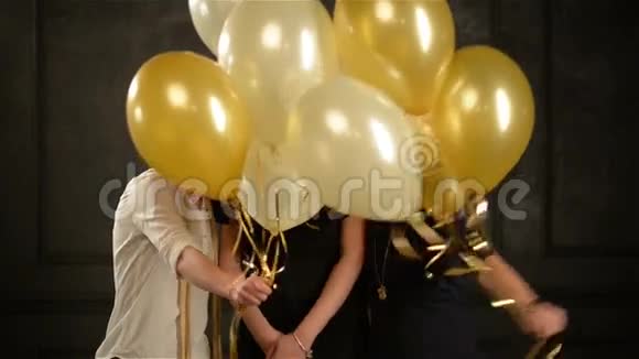 三个女孩躲在金色和白色气球后面然后突然出现和微笑广泛地看着镜头视频的预览图