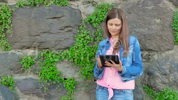 穿着棉夹克的漂亮女孩用平板电脑背景中野生石头的复古墙视频的预览图