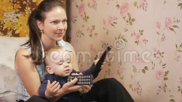 年轻的女人和她的儿子坐在家里的沙发上用电视上的遥控器仔细看屏幕视频的预览图