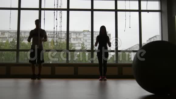 健身馆里的健身运动的女人和肌肉靠近窗户的绳子上剪影视频的预览图