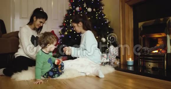 快乐的姐妹在圣诞树附近为父母包装圣诞礼物可爱的儿子吃苹果看着远处红色视频的预览图